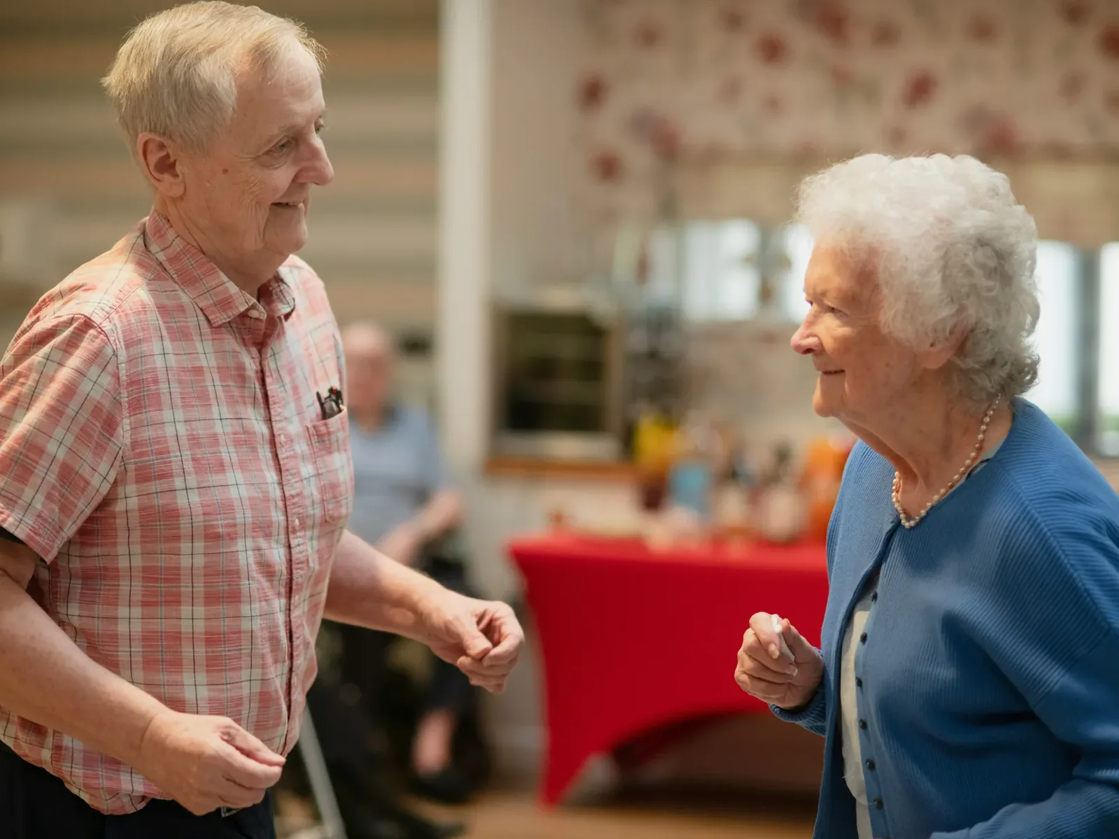 Residents and a facilitator up on their feet, moving together to live music in a care-home lounge
