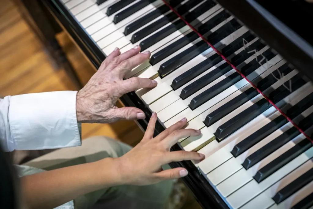 An older hand and a younger hand playing the piano together